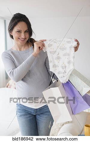 Stock Image - Pregnant Caucasian woman shopping for baby clothing. Fotosearch