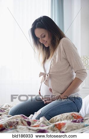 Stock Image - Pregnant Caucasian woman sitting on bed. Fotosearch