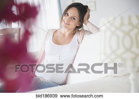 Stock Photo - Pregnant Caucasian woman sitting on sofa. Fotosearch