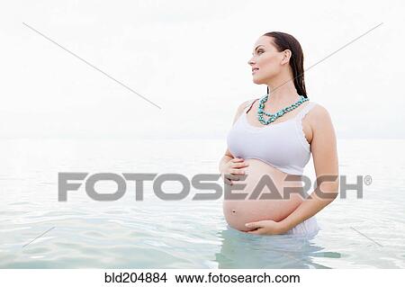 Picture - Pregnant Caucasian woman standing in water. Fotosearch