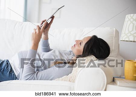 Stock Image - Pregnant Caucasian woman using digital tablet on sofa. Fotosearch