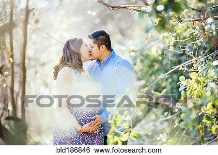 Stock Photograph - Pregnant Hispanic couple kissing outdoors. Fotosearch