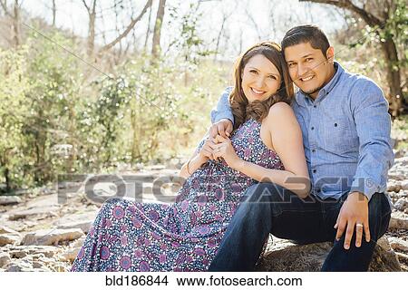 Picture - Pregnant Hispanic couple smiling outdoors. Fotosearch