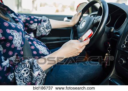 Stock Photo - Pregnant Hispanic woman using cell phone and driving. Fotosearch