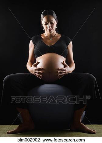 Stock Image - Pregnant Middle Eastern woman sitting on exercise ball. Fotosearch