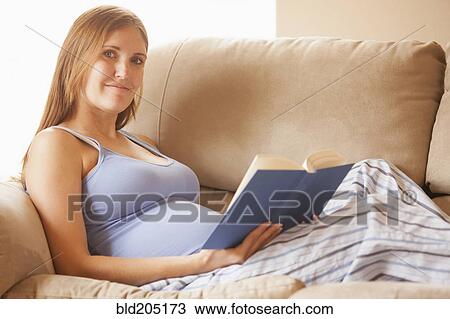 Stock Image - Pregnant woman reading on sofa. Fotosearch