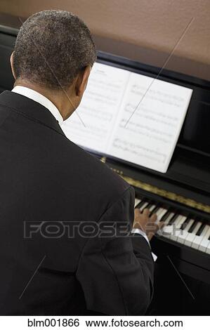 Stock Photograph - Rear view of African man playing piano. Fotosearch