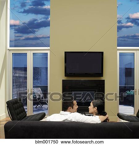 Stock Image - Rear view of Asian couple on sofa. Fotosearch
