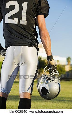 Stock Image - Rear view of football player holding helmet. Fotosearch