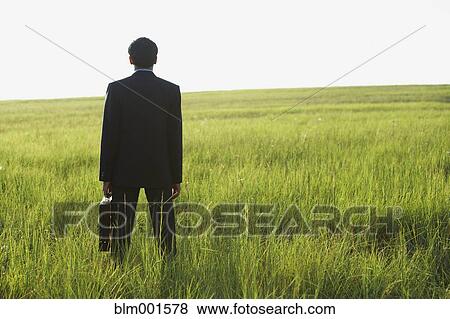 Stock Photo - Rear view of Indian businessman with briefcase in field. Fotosearch