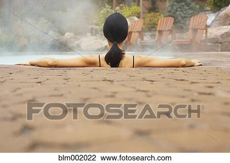 Stock Image - Rear view of woman sitting in hot tub. Fotosearch