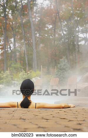 Stock Image - Rear view of woman sitting in hot tub. Fotosearch