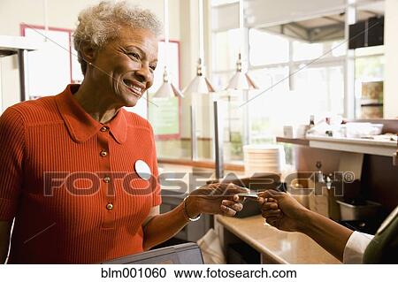 Stock Image - Senior African clerk taking customerÆs credit card. Fotosearch