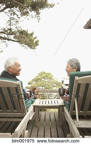 Stock Photography - Senior Asian couple drinking coffee and talking outdoors. Fotosearch