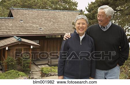 Stock Image - Senior Asian couple smiling and hugging outdoors. Fotosearch