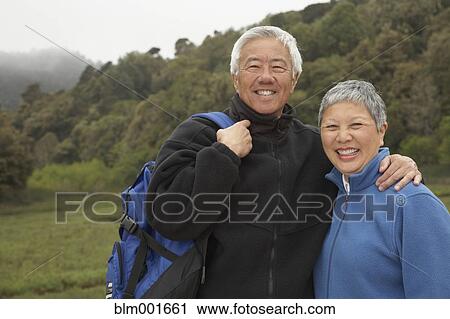 Stock Image - Senior Asian couple with backpack outdoors. Fotosearch