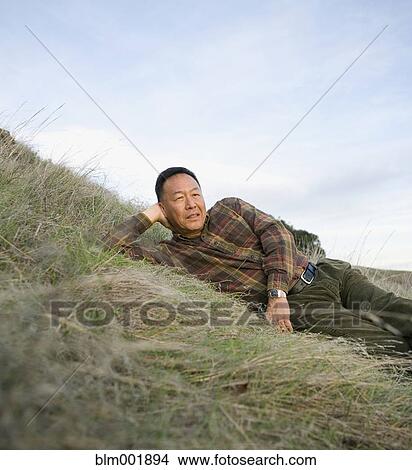 Picture - Senior Asian man laying on hillside. Fotosearch