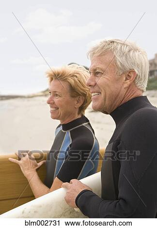 Stock Image - Senior couple carrying surfboards at beach. Fotosearch