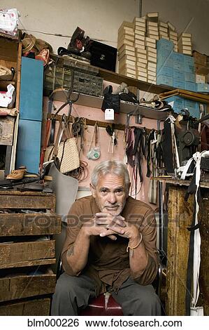 Stock Photograph - Senior Hispanic male cobbler sitting in workshop. Fotosearch