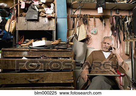 Stock Photography - Senior Hispanic male cobbler talking on cell phone. Fotosearch