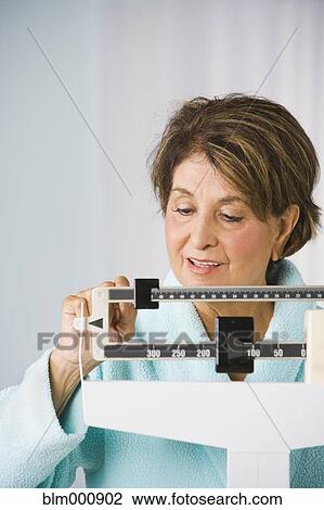 Stock Image - Senior Hispanic woman checking weight on scale. Fotosearch