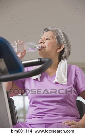 Picture - Senior Hispanic woman drinking water after workout. Fotosearch