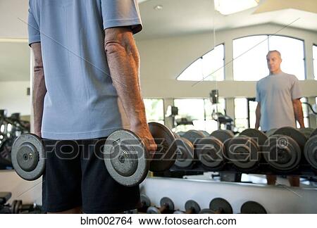 Picture - Senior man lifting weights at health club. Fotosearch