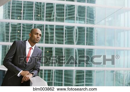 Stock Image - Serious African businessman leaning on railing of urban balcony. Fotosearch