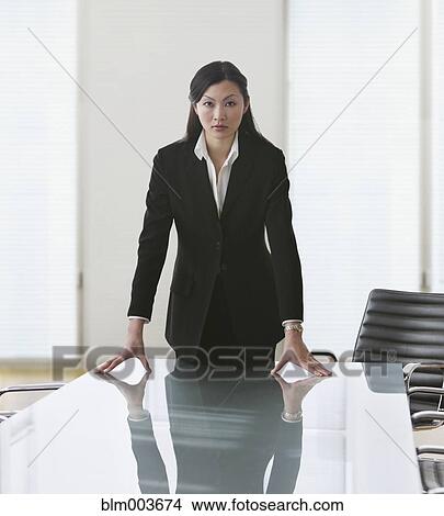 Picture - Serious Chinese businesswoman leaning on conference table. Fotosearch
