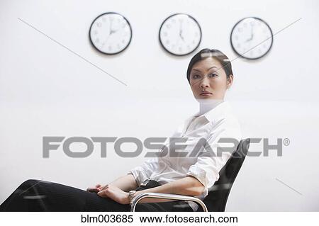 Stock Photography - Serious Chinese businesswoman sitting under clocks. Fotosearch