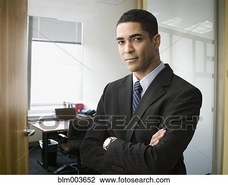 Stock Image - Serious mixed race businessman standing with arms crossed. Fotosearch