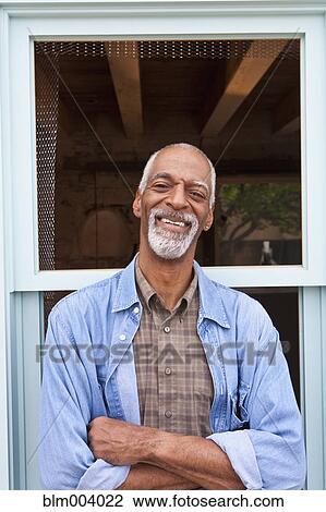 Stock Image - Smiling African man standing in front of window frame. Fotosearch