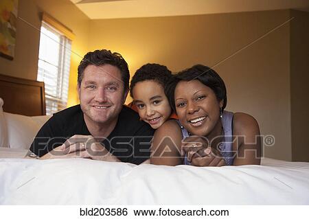 Smiling family laying on bed View Large Photo Image Stock Photograph - Smiling family laying on bed. Fotosearch