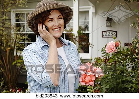 Stock Image - Smiling woman talking on cell phone in garden. Fotosearch