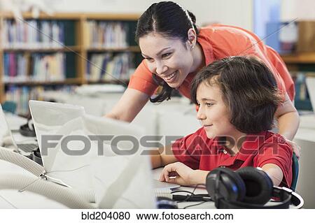 Stock Image - Teacher and student using laptop in library. Fotosearch