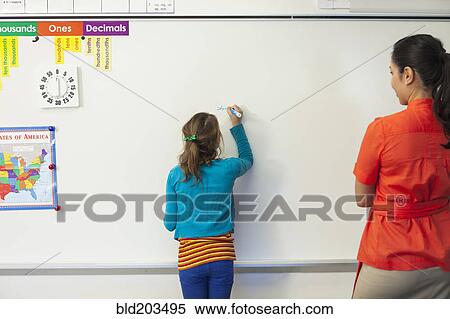 Stock Photography - Teacher watching student write on whiteboard in classroom. Fotosearch