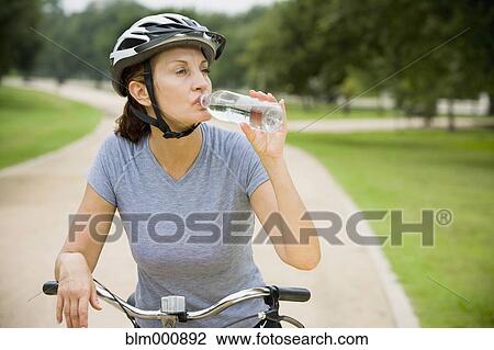 Stock Image - Thirsty mixed race woman riding bicycle. Fotosearch
