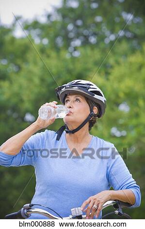 Stock Photo - Thirsty senior Hispanic woman riding bicycle. Fotosearch