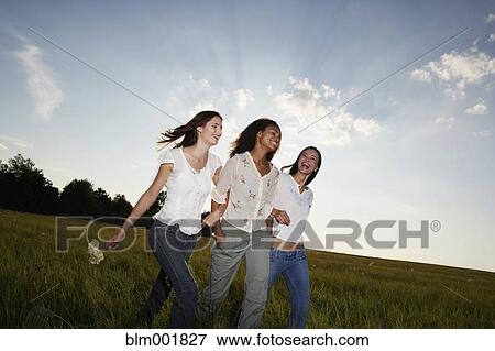 Three women walking arm in arm through meadow View Large Photo Image Stock Photo - Three women walking arm in arm through meadow. Fotosearch