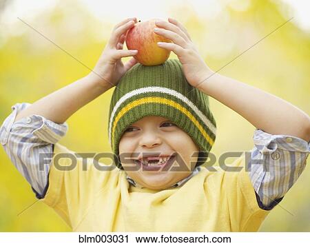 Stock Image - Toothless Hispanic boy balancing apple on head. Fotosearch