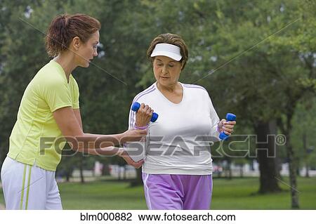 Trainer helping senior women lift hand weights View Large Photo Image Stock Image - Trainer helping senior women lift hand weights. Fotosearch