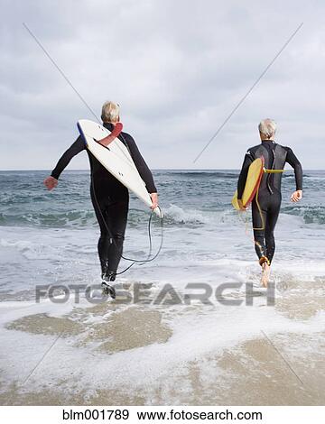 Stock Photo - Two men walking into ocean with surfboards. Fotosearch