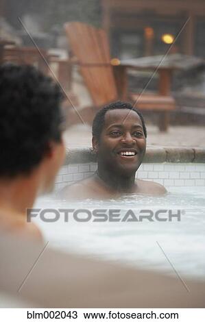 Stock Image - Two multi-ethnic men sitting in hot tub. Fotosearch