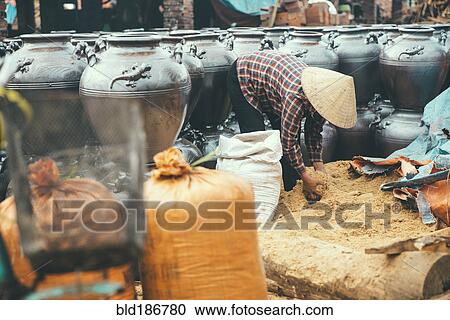 Stock Image - Vendor lifting grain into pots in market. Fotosearch
