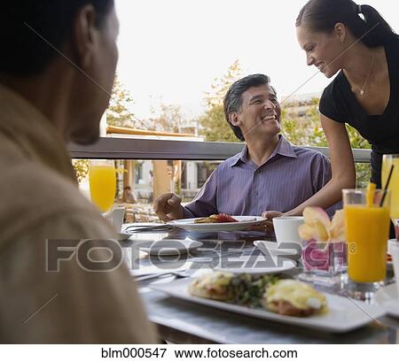 Stock Photo - Waitress serving food to man in restaurant. Fotosearch