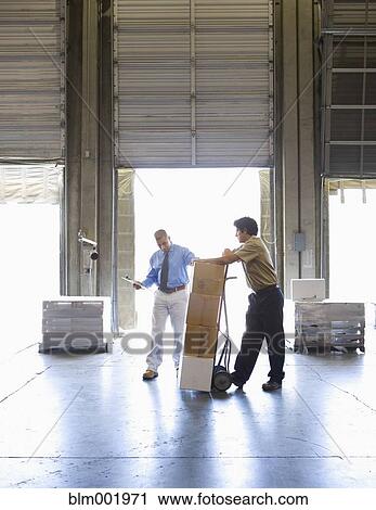 Stock Image - Warehouse worker and boss with stack of boxes. Fotosearch