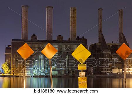 Stock Image - Warning signs and factory smokestacks lit up at night. Fotosearch
