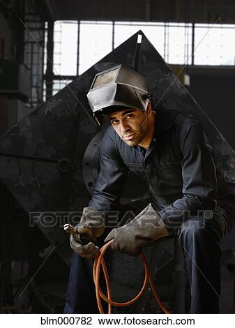 Stock Image - Welder in helmet and gloves in warehouse. Fotosearch