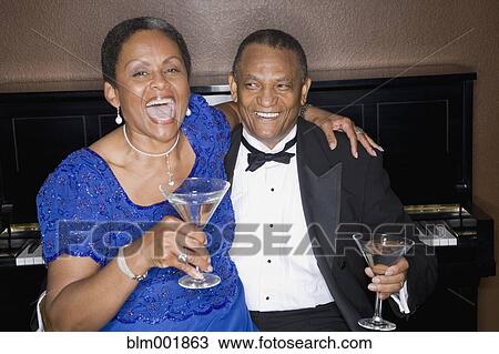 Stock Image - Well dressed african couple drinking cocktails in front of piano. Fotosearch