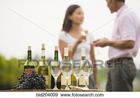 Stock Photo - Wine bottle, grapes and glasses on table outdoors. Fotosearch